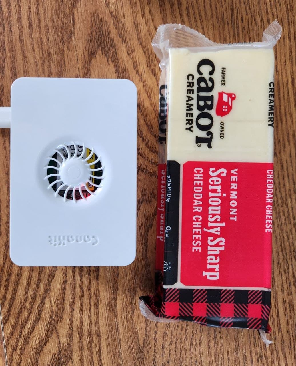 A Raspberry Pi 5 in its white case beside a block of Cabot Vermont sharp cheddar of roughly the same size